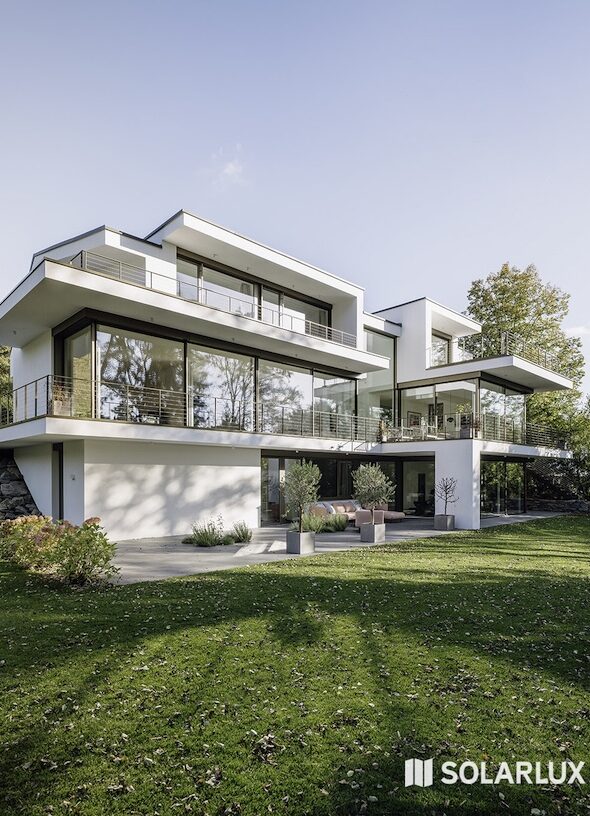 Többszintes, modern villaépület üvegezett homlokzattal, nagy felületű tolóajtókkal és ápolt zöld kerttel